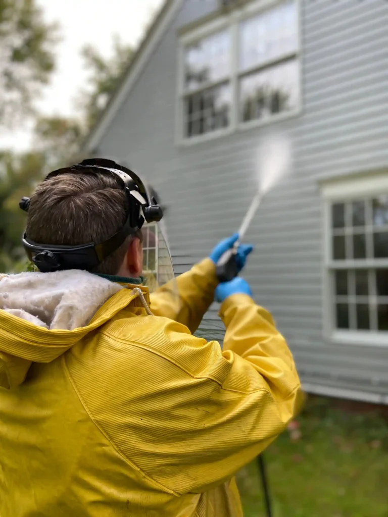 Technician in yellow jacket pressure washing home